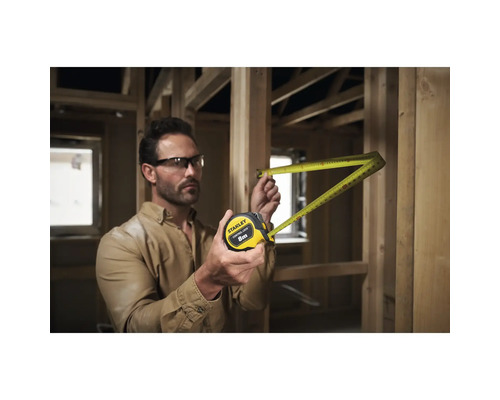 Un homme mesure avec un mètre à ruban Stanley de 8 m dans une construction brute.