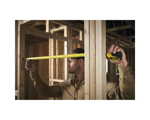 Un artisan mesure avec un mètre ruban dans une construction brute