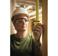 Femme avec lunettes de protection et casque de chantier mesurant avec un mètre ruban Stanley.