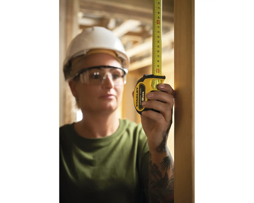 Femme avec lunettes de protection et casque de chantier mesurant avec un mètre ruban Stanley.