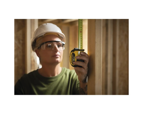 Une femme mesure avec un mètre ruban Stanley de 8 m dans une construction à ossature bois