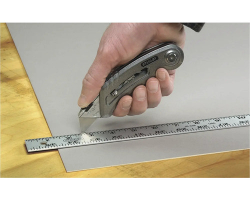 Main coupant un matériau avec un cutter Stanley et une règle