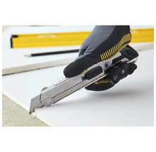 Eine Hand mit Arbeitshandschuh schneidet mit einem Cuttermesser eine Gipskartonplatte.