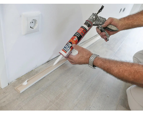 Application de colle de montage pour fixer une plinthe à un mur