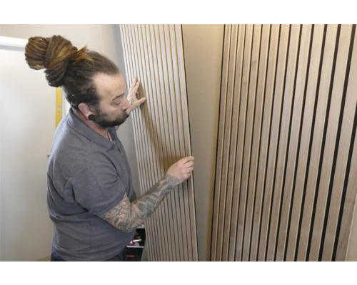 Un homme installe des panneaux acoustiques au mur pour l'absorption du son