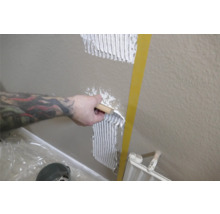 Une personne applique de la colle à carrelage sur un mur à l'aide d'une spatule.