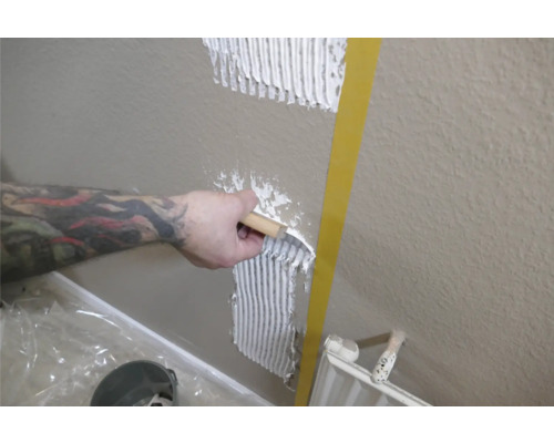 Une personne applique de la colle à carrelage sur un mur à l'aide d'une spatule.