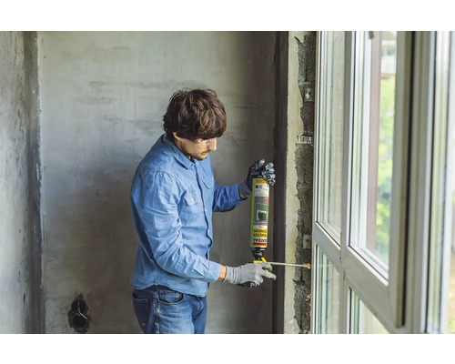 Mann dämmt Fenster mit Montageschaum