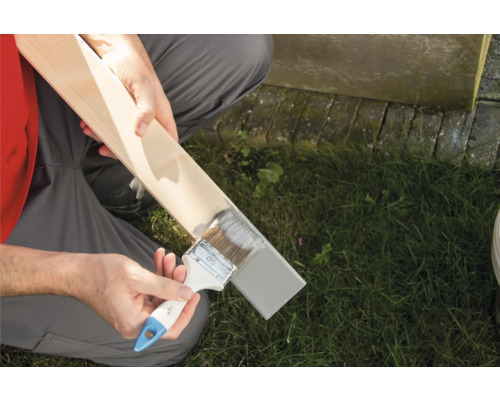 Une personne peint une planche de bois avec un pinceau.