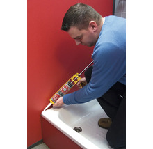 Une personne utilise un pistolet à cartouche pour sceller un joint entre un receveur de douche et un mur.