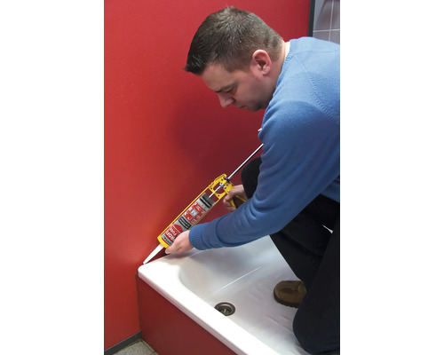 Eine Person verwendet eine Kartuschenpistole, um eine Fuge zwischen einer Duschwanne und einer Wand zu versiegeln.