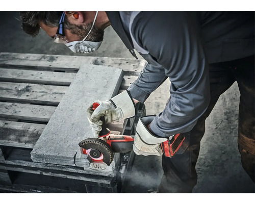 Eine Person schneidet mit einer Flex Steine, wobei sie Schutzkleidung trägt.