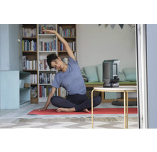 Szene eines Wohnzimmers mit einer Frau beim Yoga und einer tragbaren Heizung auf einem Tisch.