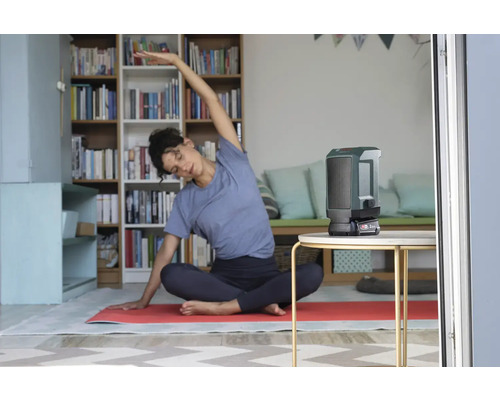 Szene eines Wohnzimmers mit einer Frau beim Yoga und einer tragbaren Heizung auf einem Tisch.