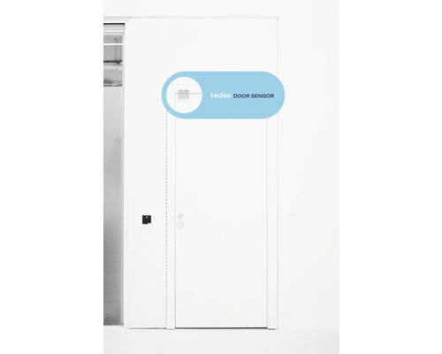 Capteur de porte Tedee monté sur le coin supérieur d'une porte blanche dans une pièce lumineuse.