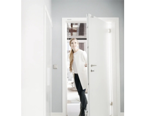 Une femme ouvre une porte d entrée d appartement blanche avec verrouillage multipoints dans une pièce moderne et lumineuse.
