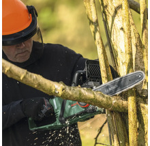 Une personne coupe des branches avec une tronçonneuse à batterie Bosch, tout en portant des lunettes de protection et un casque.