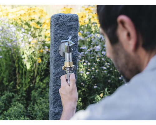 Gartenszene mit Wasserhahn an Steinsäule und Person, die einen Schlauch anschliesst