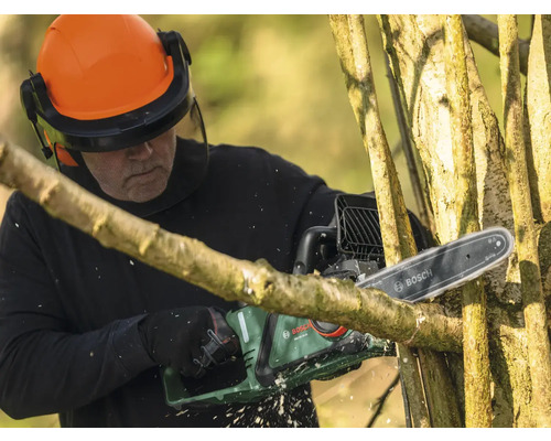 Homme avec casque de protection et tronçonneuse Bosch coupant un arbre