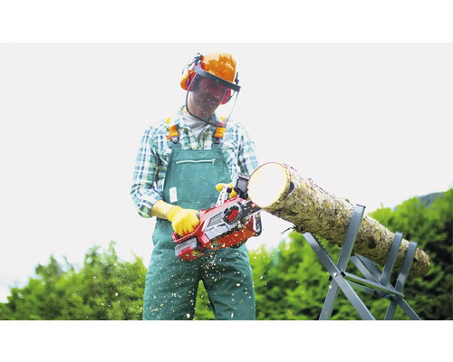 Un homme coupe du bois avec une tronçonneuse sur un chevalet de sciage, il porte des vêtements de protection