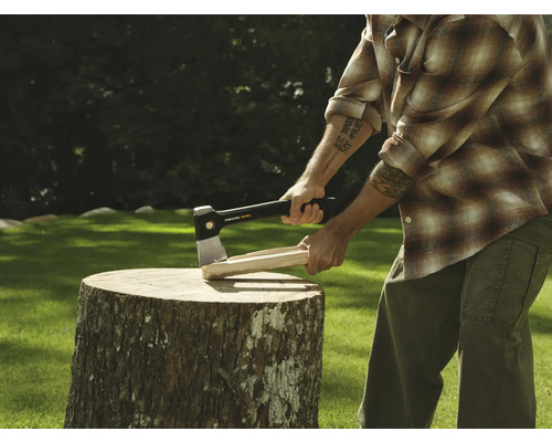 Mann spaltet Holz mit einer Axt auf einem Baumstumpf.