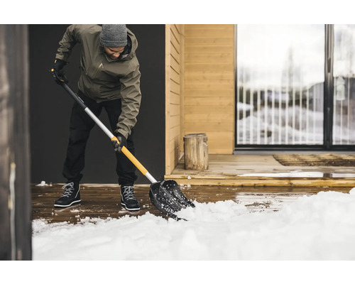 Mann schaufelt Schnee mit einer Schneeschaufel vor einem Haus.