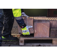 Eine Person in Arbeitskleidung und Arbeitshandschuhen hebt einen Ziegelstein von einer Holzpalette.