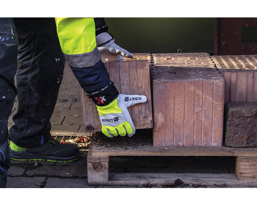 Eine Person in Arbeitskleidung und Arbeitshandschuhen hebt einen Ziegelstein von einer Holzpalette.