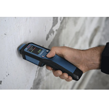 Hand hält ein Feuchtigkeitsmessgerät zur Messung der Wandfeuchtigkeit.