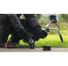 Une personne remplace la lame d'un coupe-bordure, avec une batterie et une bobine à proximité.