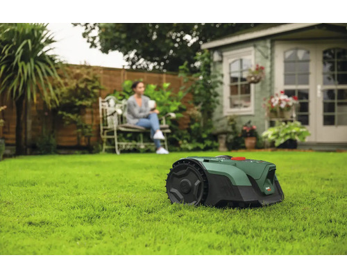 Szene mit Rasenmähroboter auf Rasen und einer Frau, die auf einer Bank sitzt