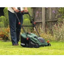 Une personne utilise une tondeuse à gazon Bosch verte sur une pelouse.
