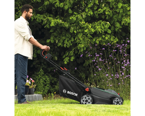Un homme utilise une tondeuse à gazon dans le jardin. Logo Bosch.