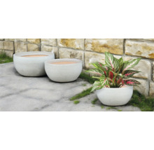 Drei runde Pflanzgefäße im Außenbereich vor einer Steinmauer.