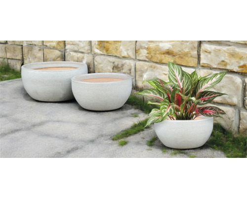 Drei runde Pflanzgefäße im Außenbereich vor einer Steinmauer.