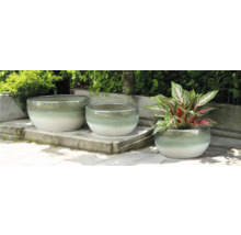 Trois pots de fleurs ronds en céramique sur une terrasse en pierre, dont un avec une plante.