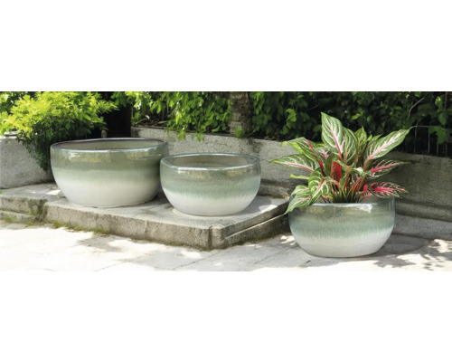 Trois pots de fleurs ronds en céramique sur une terrasse en pierre, dont un avec une plante.