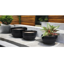 Drei schwarze Pflanzgefäße unterschiedlicher Größe auf einer Steinstufe mit Pflanzen
