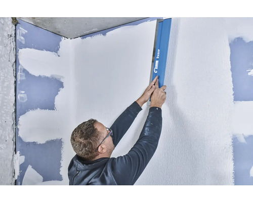 Un homme lisse un mur avec une lisseuse de Knauf