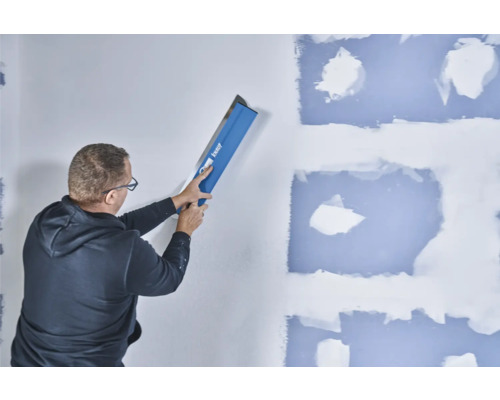 Un homme lisse un mur avec une spatule à lisser Knauf