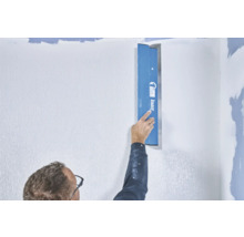 Une personne lisse un mur avec une spatule de Knauf
