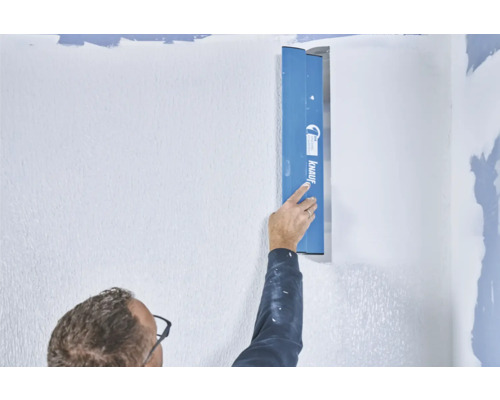Une personne lisse un mur avec une spatule de Knauf