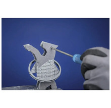 Un homme ganté retire les structures de support d'un objet imprimé en 3D à l'aide d'un tournevis.