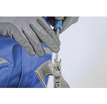 Une personne lime une grille d'aération avec une lime à clé, protégée par des gants de travail.