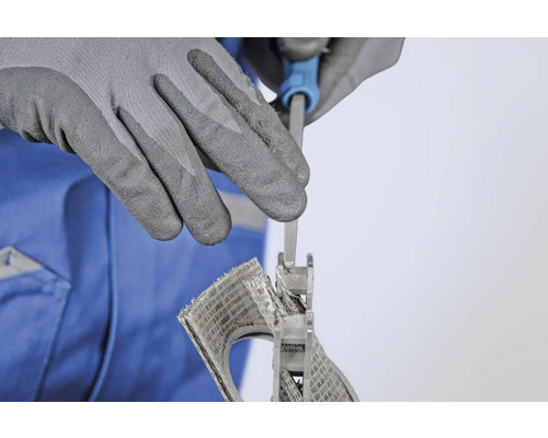 Une personne lime une grille d'aération avec une lime à clé, protégée par des gants de travail.