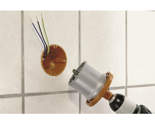 Diamant-Lochsäge bohrt Loch in geflieste Wand neben einer Unterputzdose mit Kabeln