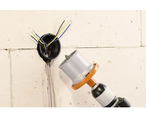 Bohrmaschine mit Bohrkrone neben einer Wandsteckdose mit Kabeln