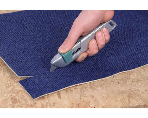 Eine Hand schneidet mit einem Teppichmesser einen Teppich.