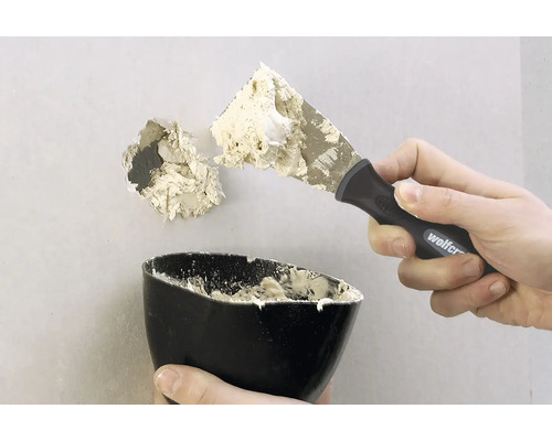 Ein Loch in einer Wand wird mit einem Spachtel und Spachtelmasse repariert.
