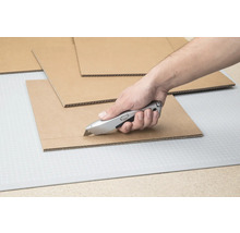 Main coupant du carton avec un cutter sur un tapis de découpe